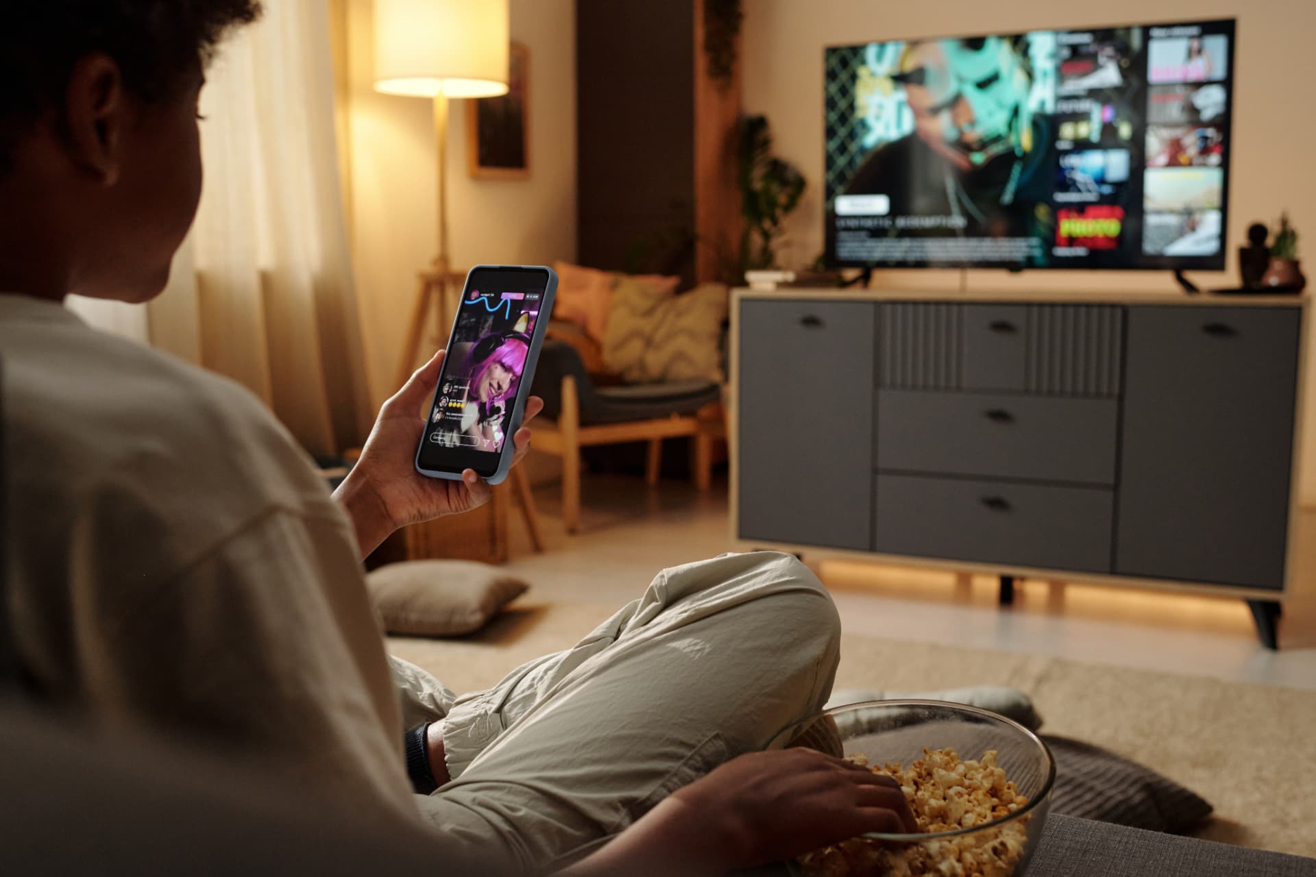 Person relaxing on a couch with a phone while a TV plays in the background
